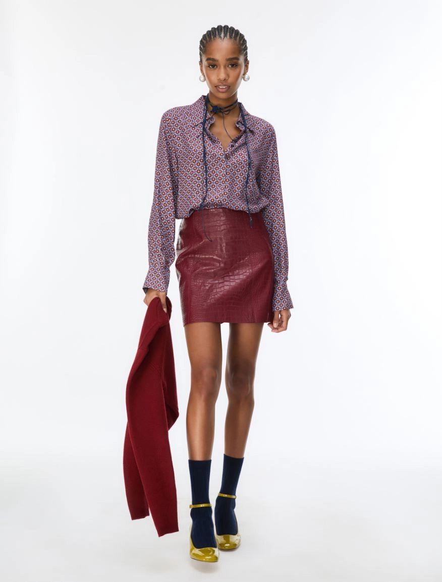 woman wearing a blue and red pattern shirt and red skirt holding a red jacket on a white background