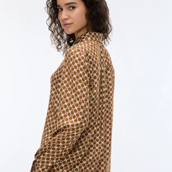 woman wearing a geometric brown and cream shirt on a white background rear view