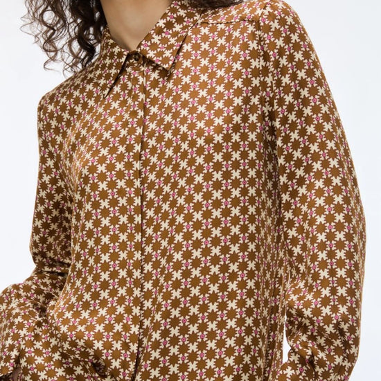 A close-up of a model wearing a brown long-sleeve collared shirt with a repeating cream floral pattern, set against a plain light gray background.