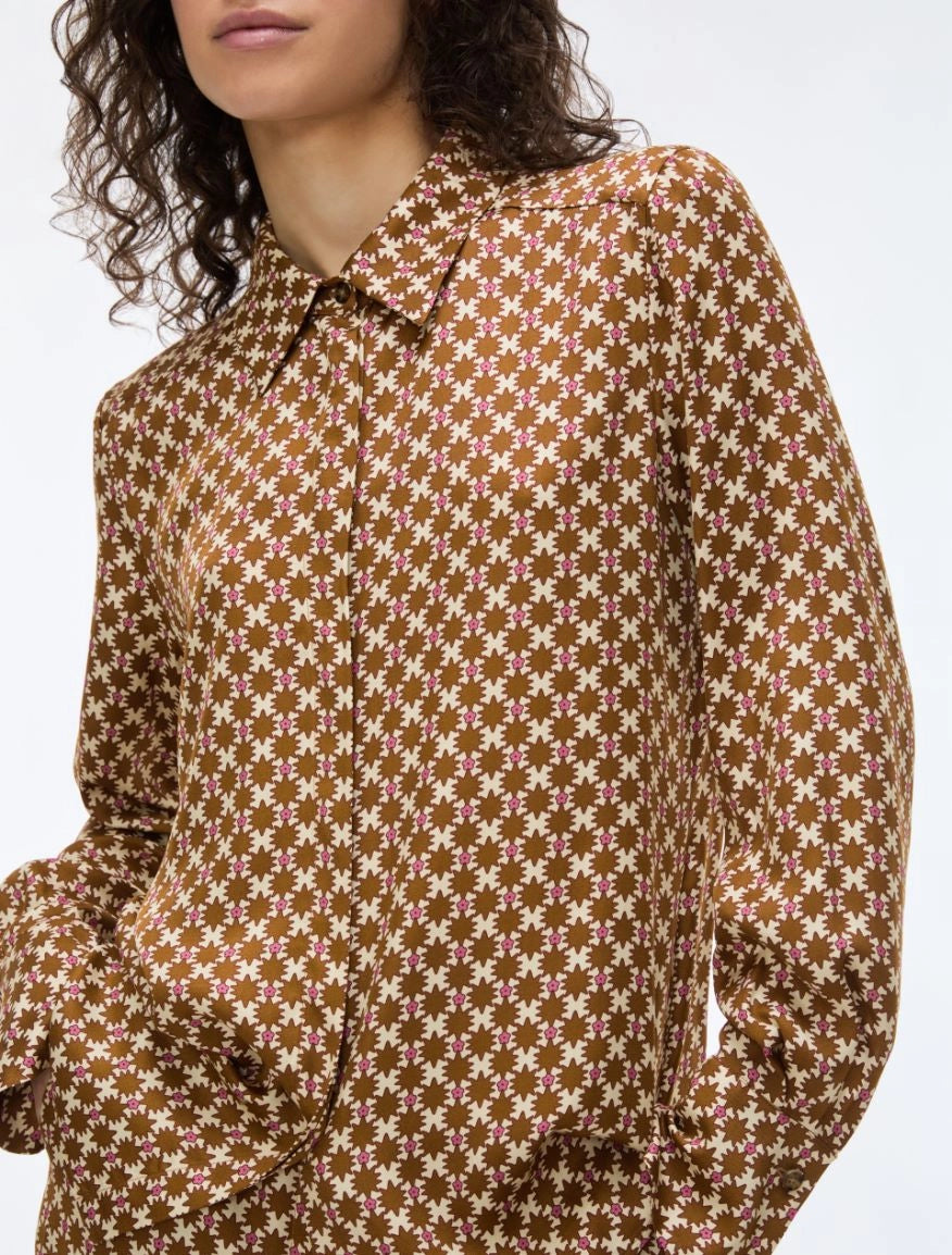 A close-up of a model wearing a brown long-sleeve collared shirt with a repeating cream floral pattern, set against a plain light gray background.