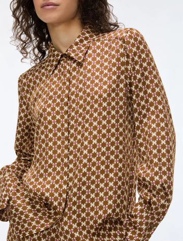 A close-up of a model wearing a brown long-sleeve collared shirt with a repeating cream floral pattern, set against a plain light gray background.