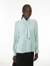 A model wearing a pale mint green long-sleeve blouse with a high gathered collar and a large front bow, paired with a black skirt, against a plain white studio background.