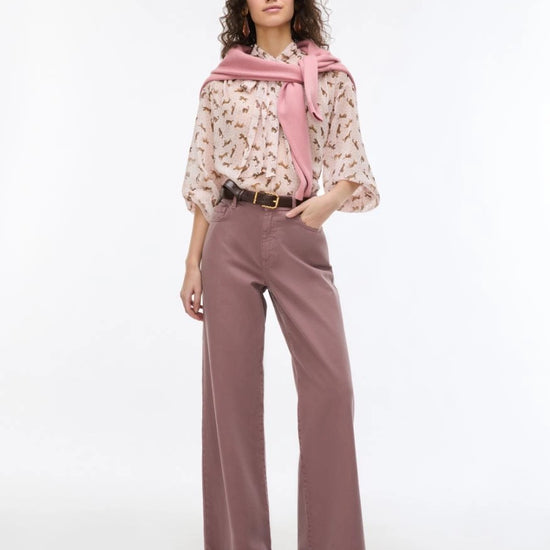 Woman wearing a patterned blouse, pink scarf, and wide-leg pants on a white background