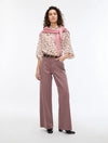 Woman wearing a patterned blouse, pink scarf, and wide-leg pants on a white background