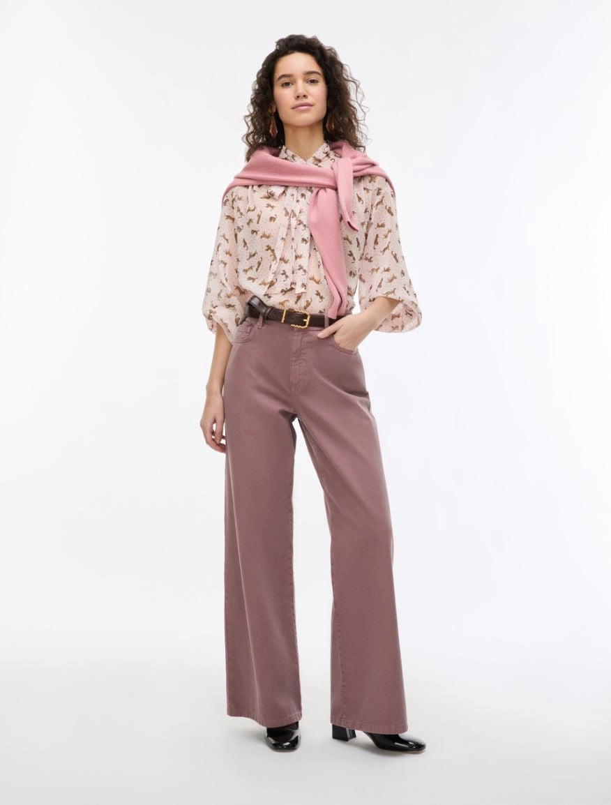 Woman wearing a patterned blouse, pink scarf, and wide-leg pants on a white background