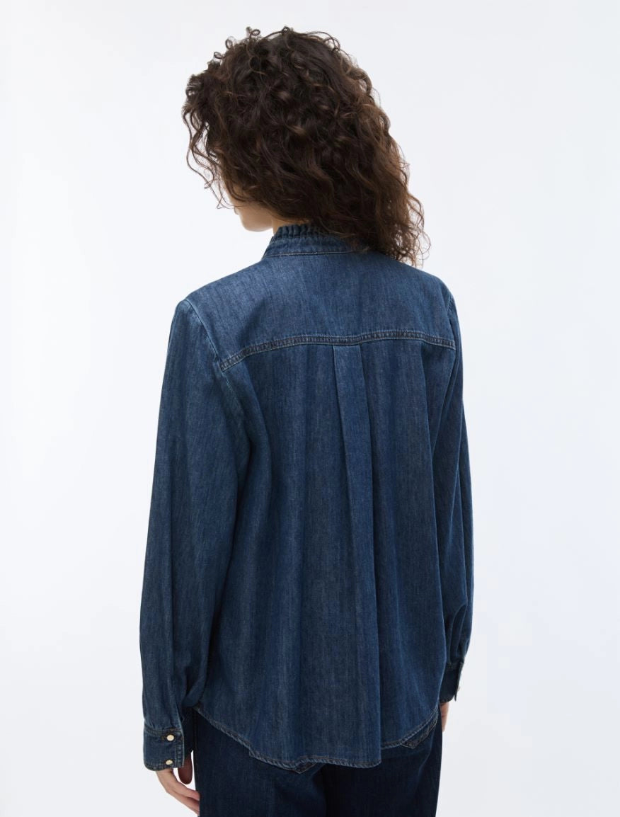 A person shown from the back wearing a dark blue denim long-sleeve button-up shirt and dark jeans against a plain white studio background.