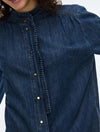 A model wearing a dark blue denim button-up shirt, matching wide-leg jeans, a brown belt, and holding a black leather jacket against a plain white studio background CLOSE UP