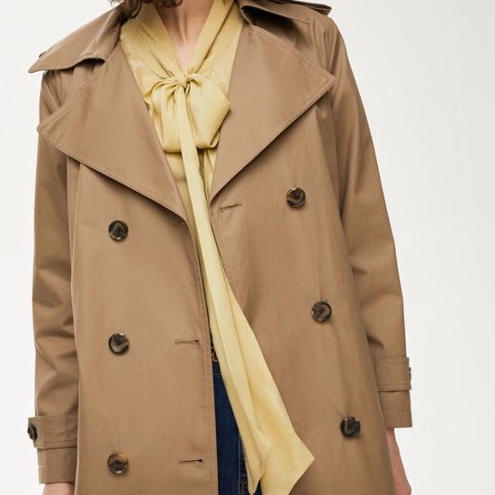 Person wearing a beige trench coat over a yellow top on a white background