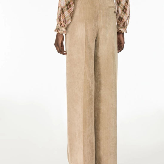 A model shown from the back wearing high-waisted, wide-leg taupe pants and a brown and beige plaid shirt, photographed against a clean white studio background.