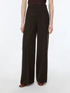 A model wearing high-waisted, wide-leg dark brown trousers, paired with a dark brown top and brown flat shoes, photographed against a clean white studio background.