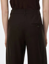 Close-up back view of a person wearing dark brown tailored trousers with a welt pocket and a small metallic button detail, paired with a dark top against a light gray background.
