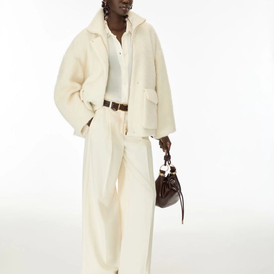 Woman wearing cream fur jacket and trousers on a white background