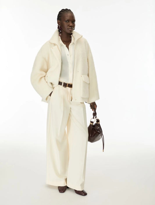 Woman wearing cream fur jacket and trousers on a white background