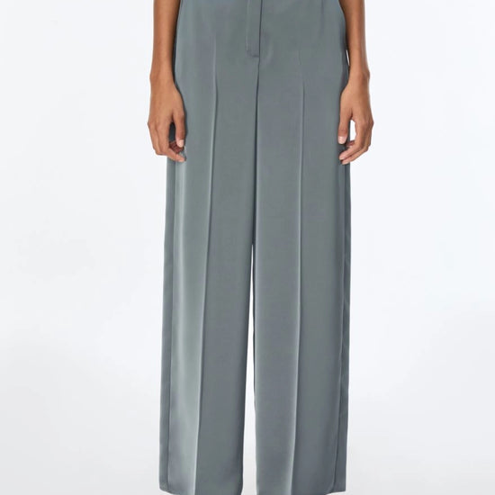 A model wearing slate blue wide-leg trousers with a matching waistband, paired with silver sandals, shown from the waist down on a white studio background.