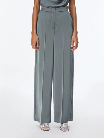 A model wearing slate blue wide-leg trousers with a matching waistband, paired with silver sandals, shown from the waist down on a white studio background.