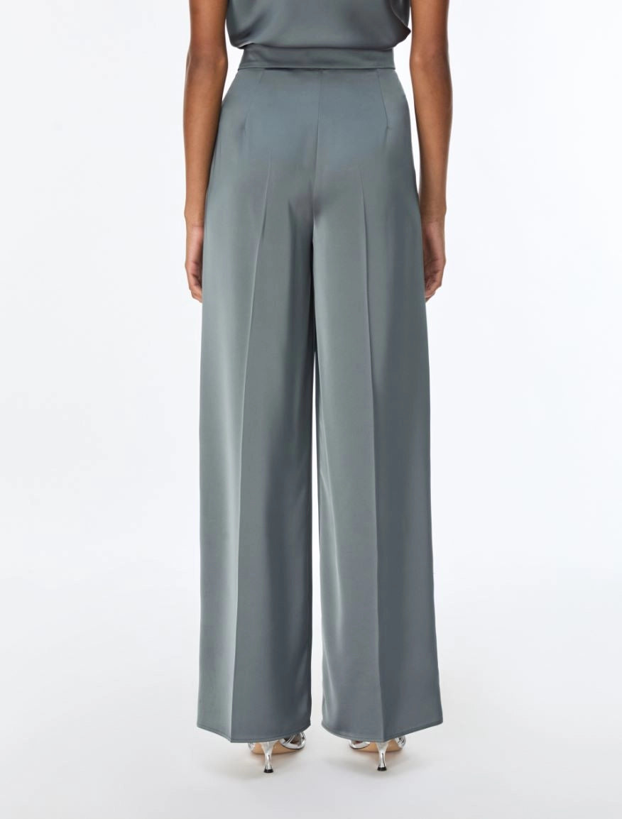 A model shown from the back wearing high-waisted, wide-leg trousers in a muted slate gray color, paired with a matching gray top and metallic heels, against a plain white studio background.