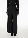A model wearing a black long-sleeve button-front top with small metallic star details on the cuffs and waist, paired with high-waisted black wide-leg trousers and black shoes, against a plain white studio background.