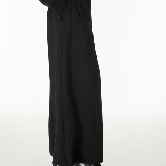 A model wearing a long black wide-leg dress with star details on the sleeves, paired with black pointed-toe heels, shown from the waist down against a plain white studio background.