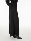 A model wearing a long black wide-leg dress with star details on the sleeves, paired with black pointed-toe heels, shown from the waist down against a plain white studio background.