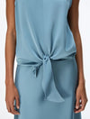 A close-up of a model wearing a light blue sleeveless top with a tied knot detail at the waist.