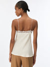 A woman shown from the back wearing a cream-colored satin camisole top with thin straps and a lace trim across the upper back, paired with tan pants, against a plain white background.