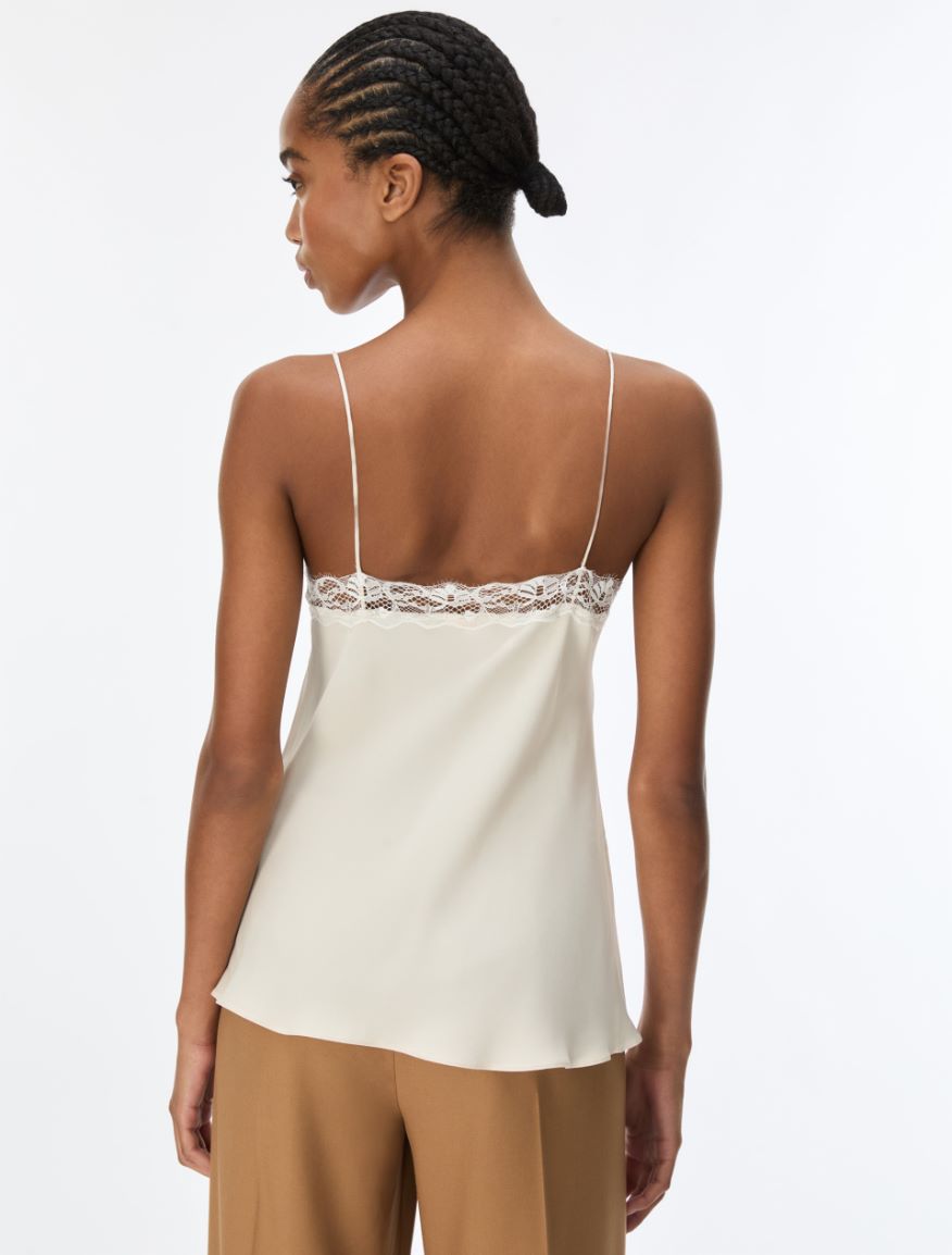 A woman shown from the back wearing a cream-colored satin camisole top with thin straps and a lace trim across the upper back, paired with tan pants, against a plain white background.