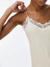 Close-up of a model wearing a cream-colored camisole with delicate white lace trim along the neckline and thin spaghetti straps.