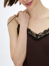 Close-up of a woman wearing a dark brown camisole with black lace trim and thin black spaghetti straps, adjusting the strap against a plain white background.