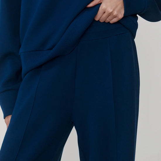Close-up of a person wearing a dark navy blue sweatshirt and matching wide-leg trousers, with the hand pulling slightly at the sweatshirt fabric.