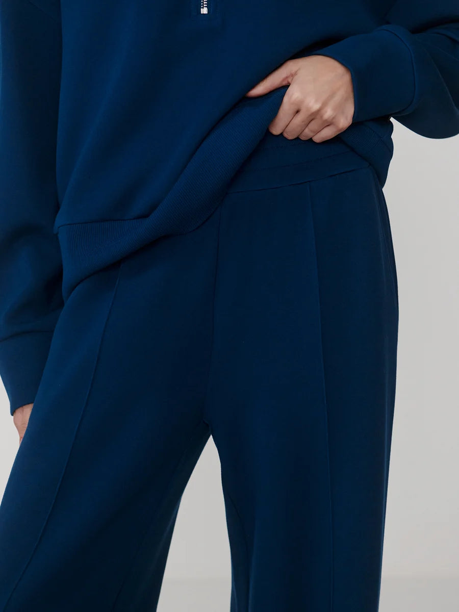 Close-up of a person wearing a dark navy blue sweatshirt and matching wide-leg trousers, with the hand pulling slightly at the sweatshirt fabric.