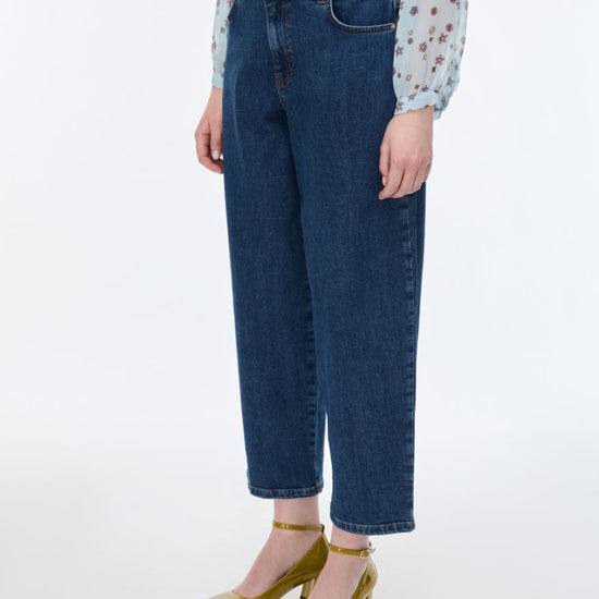 Person wearing blue jeans and a patterned top on a white background