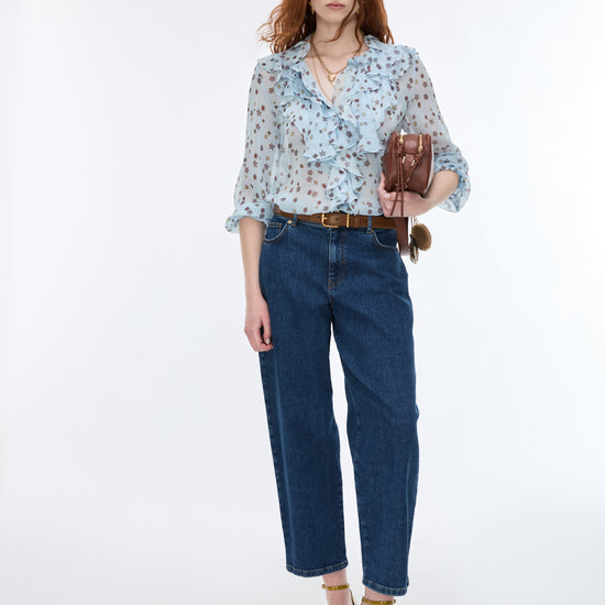 Woman wearing a light blue floral blouse and dark blue jeans on a white background