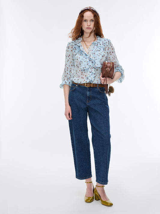 Woman wearing a light blue floral blouse and dark blue jeans on a white background
