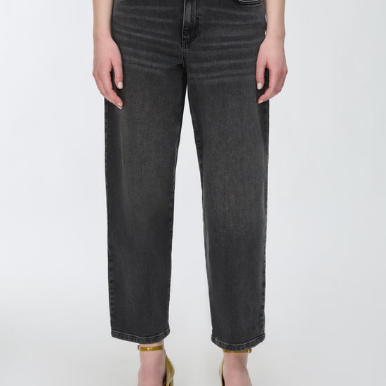 A model wearing a pair of dark gray cropped jeans with a straight-leg fit, paired with gold heels and a white top against a plain white background.