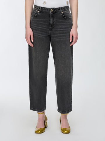 A model wearing a pair of dark gray cropped jeans with a straight-leg fit, paired with gold heels and a white top against a plain white background.