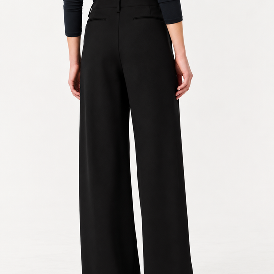 A model shown from the back wearing black wide-leg trousers and a black long-sleeve top against a plain white studio background.
