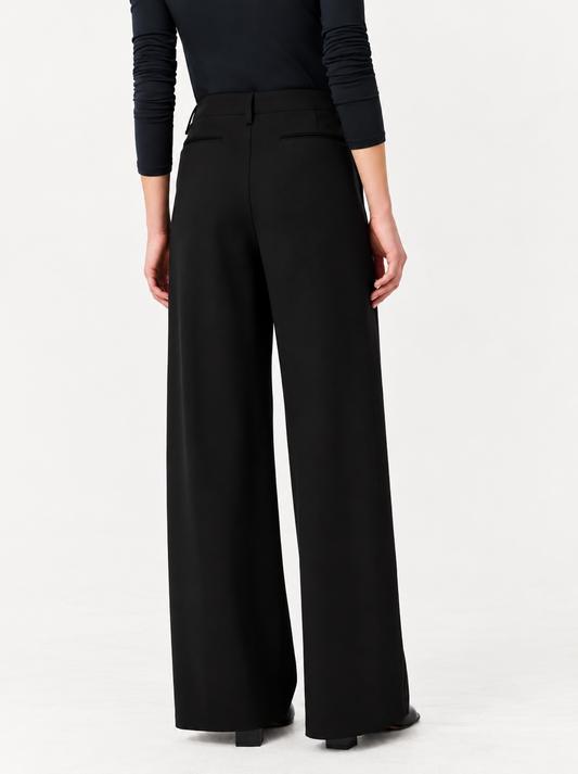 A model shown from the back wearing black wide-leg trousers and a black long-sleeve top against a plain white studio background.