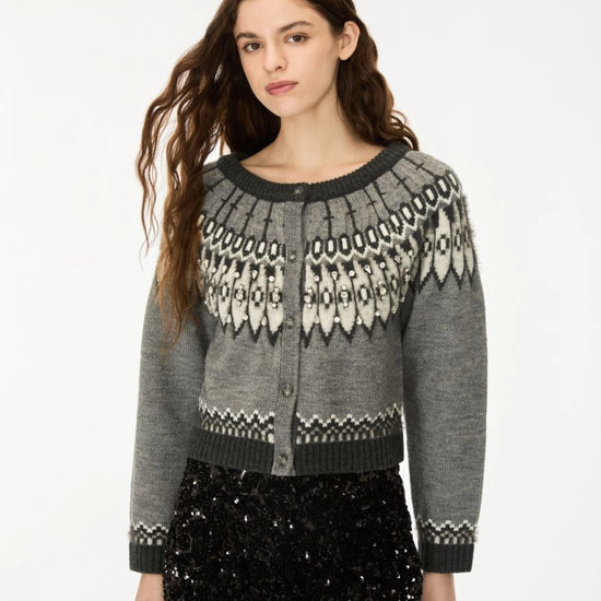 A woman modeling a gray knit cardigan with a black and white Fair Isle pattern across the yoke and cuffs, paired with black sequined pants against a plain white studio background.