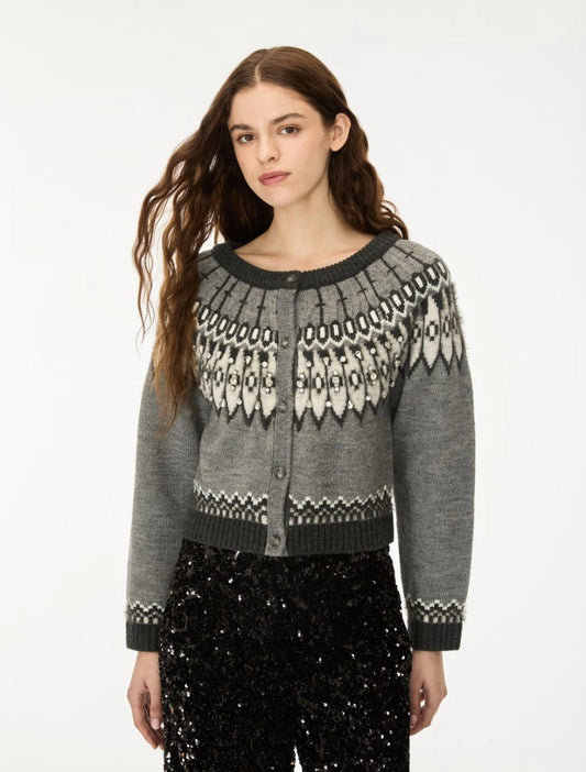 A woman modeling a gray knit cardigan with a black and white Fair Isle pattern across the yoke and cuffs, paired with black sequined pants against a plain white studio background.