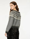 A woman wearing a gray knit sweater with a black and white Fair Isle pattern across the shoulders and sleeves, paired with a black sequined skirt, photographed against a plain white studio background.
