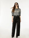 A model wearing a gray and white patterned knit cardigan with black trim, paired with black sequined wide-leg pants, sunglasses, and black shoes, photographed against a plain white studio background.