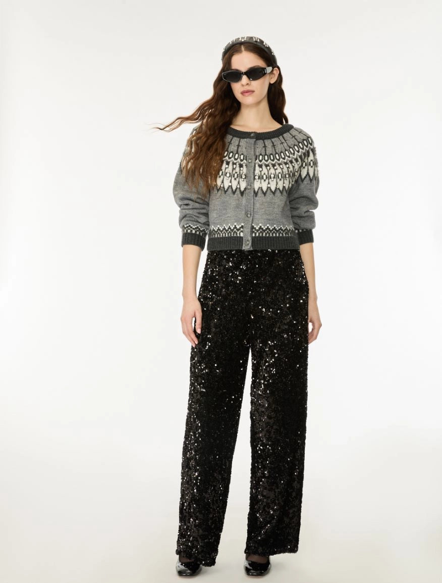 A model wearing a gray and white patterned knit cardigan with black trim, paired with black sequined wide-leg pants, sunglasses, and black shoes, photographed against a plain white studio background.