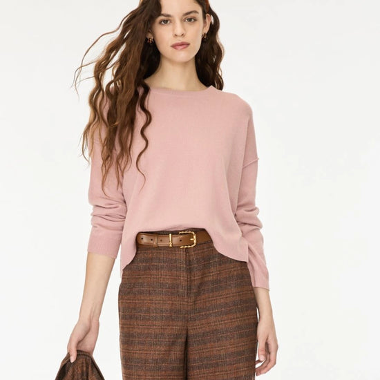 A woman modeling a dusty pink long-sleeve knit top paired with brown and beige plaid trousers, a brown belt, and a matching brown headband on a plain white studio background.