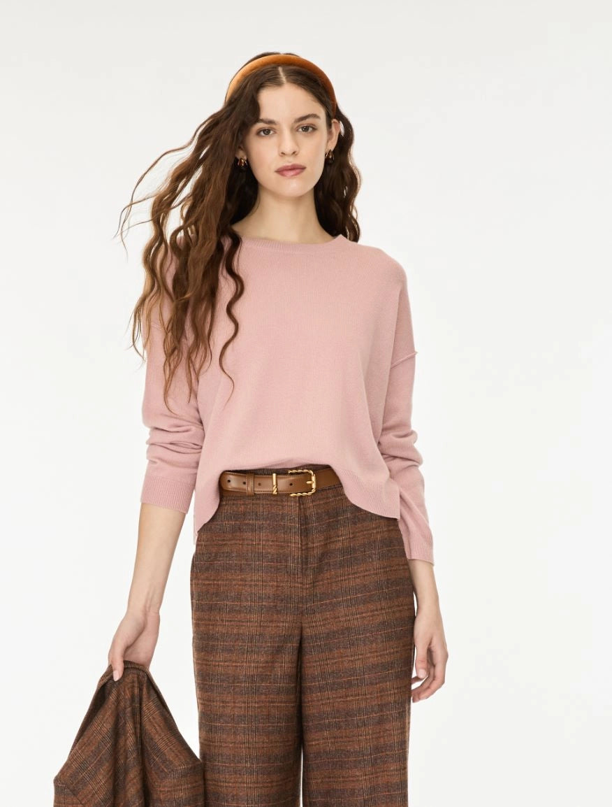 A woman modeling a dusty pink long-sleeve knit top paired with brown and beige plaid trousers, a brown belt, and a matching brown headband on a plain white studio background.