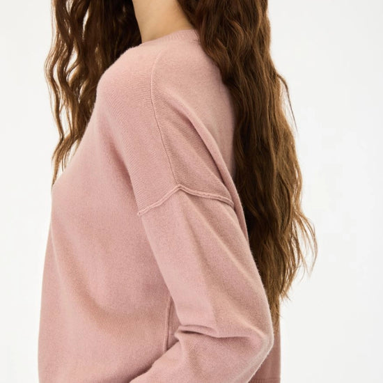 A woman wearing a dusty pink knit sweater, shown from a side-back angle against a clean white background.
