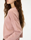 A woman wearing a dusty pink knit sweater, shown from a side-back angle against a clean white background.