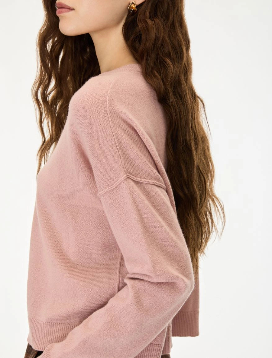 A woman wearing a dusty pink knit sweater, shown from a side-back angle against a clean white background.