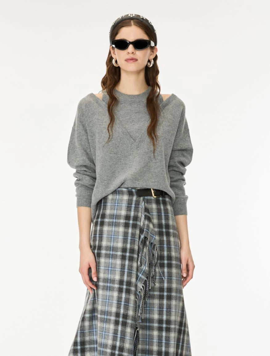 A model wearing a gray knit sweater with shoulder cutouts and a blue-gray plaid skirt, styled with black sunglasses and a headband against a plain white background.