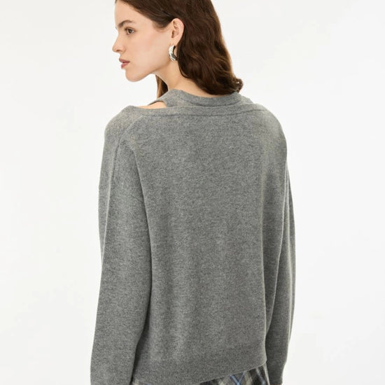 A woman shown from the back wearing a heather gray knit sweater with a wide collar and a plaid skirt, photographed against a plain light gray studio background.