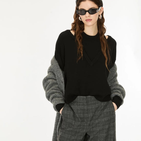 A model wearing a black knit top with gray knit sleeves, paired with gray plaid trousers, a patterned headband, and black sunglasses, against a plain white background.